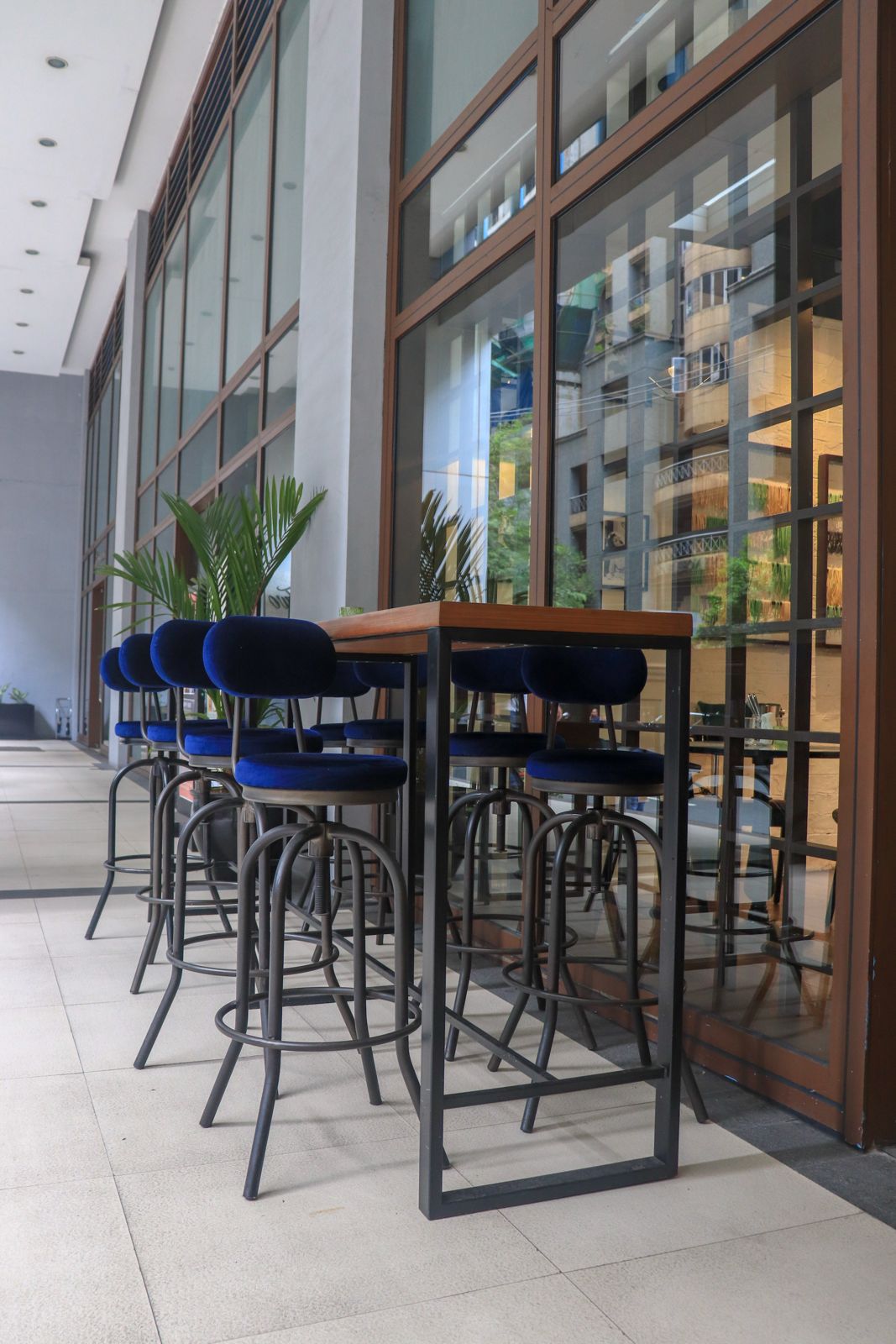Blue upholstered bar stools arranged around a high table on a restaurant terrace.